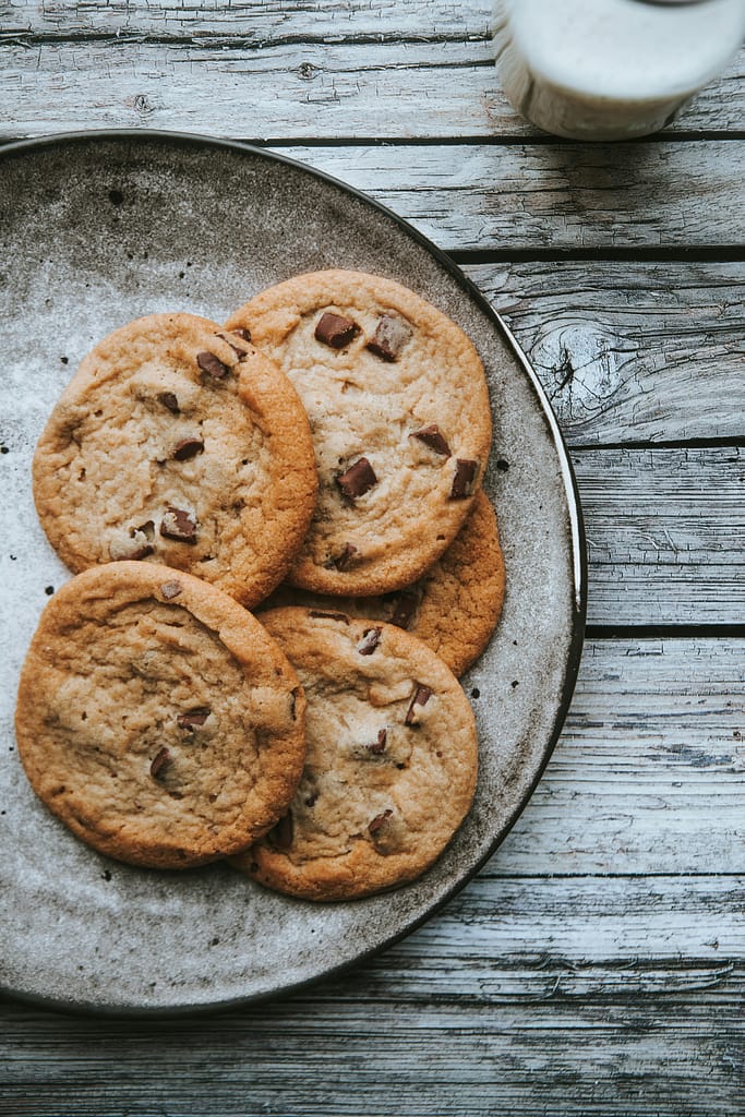 Freshly baked chocolate chip cookies arranged on a rustic plate, showcasing a homemade dessert.