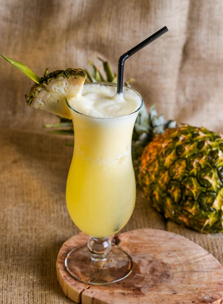 Chilled pineapple juice in a glass with a straw and sliced pineapple garnish.